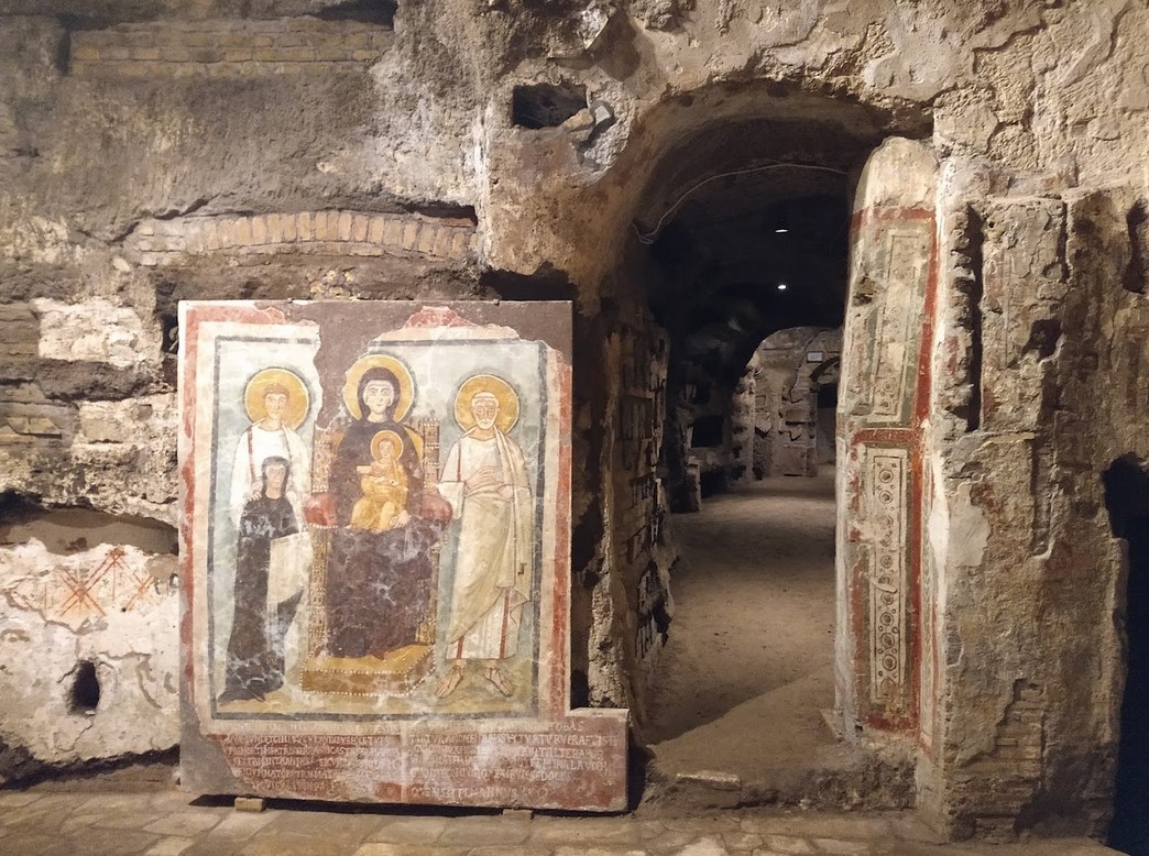Wall painting from the Catacombs of Commodilla in the so-called Tomb of Turtura, mid-6th century. The fresco depicts the Madonna and Child seated on a golden stool, with the figures of Saints Felix and Adautto and the donor, Turtura. An inscription runs along the lower border: 'Your name is Turtura, and truly you were a real turtle-dove'.